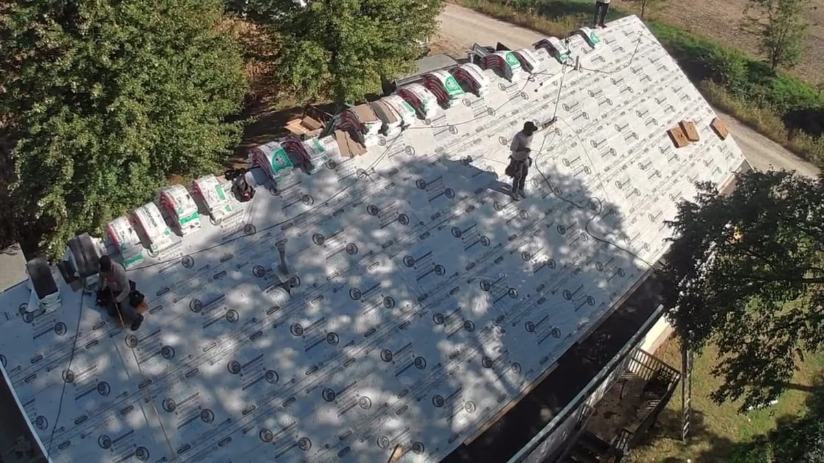 Aerial view of a roof with white underlayment and new shingles being installed, surrounded by trees and vegetation