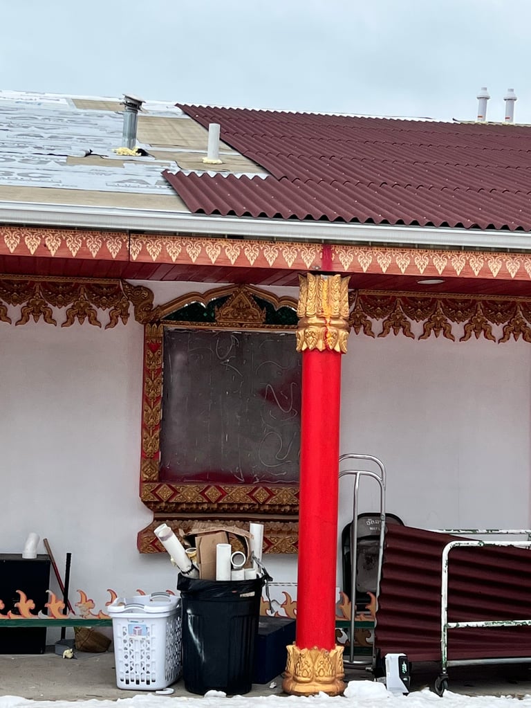 Exterior of a Southeast Asian Buddhist building with ornate red and gold trim, dark roof, and decorative wooden eaves above an entrance