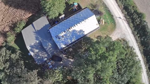 Aerial view of a blue and white rectangular swimming pool surrounded by green trees and a gravel pathway